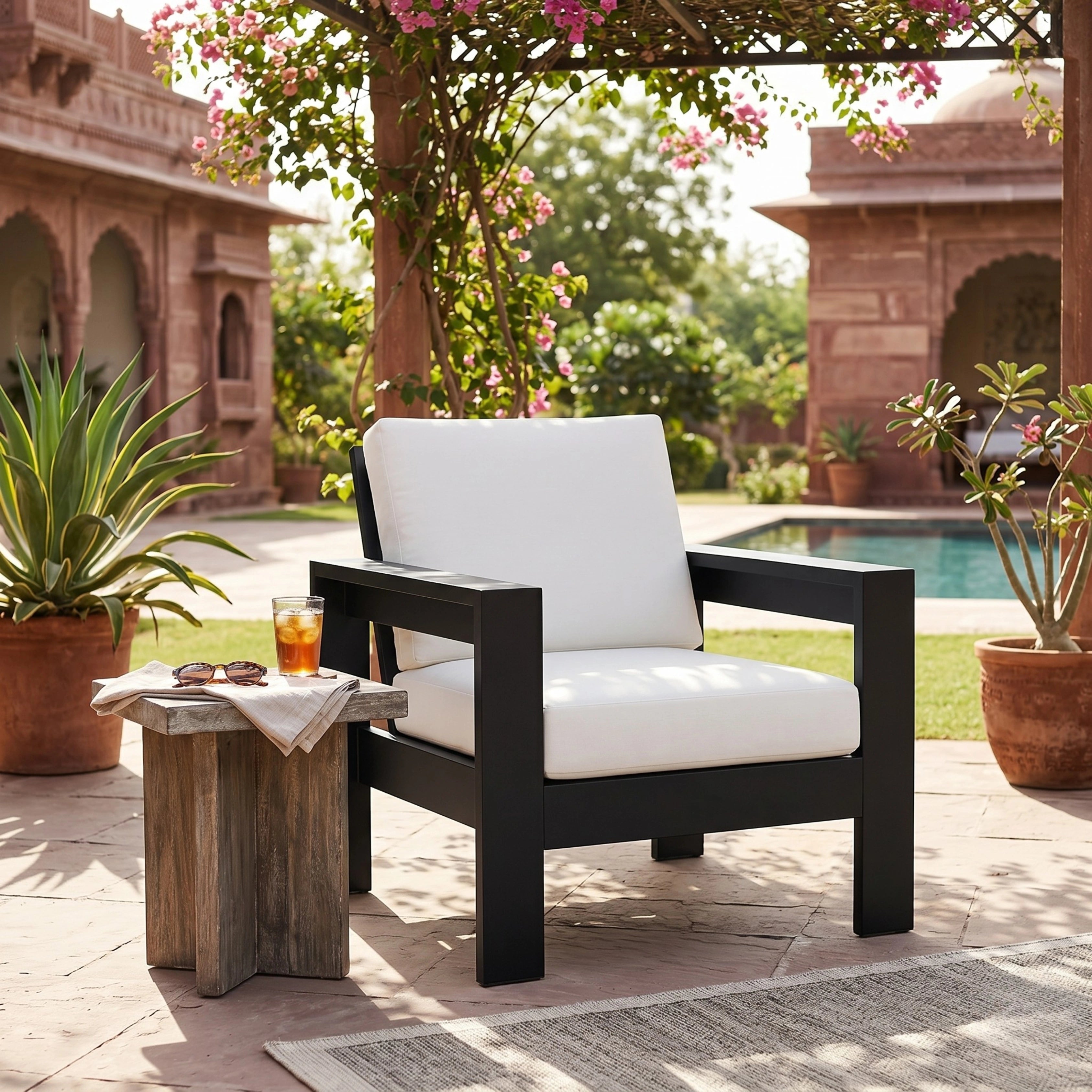 Black armchair with white cushions on a patio with a pool and garden in the background